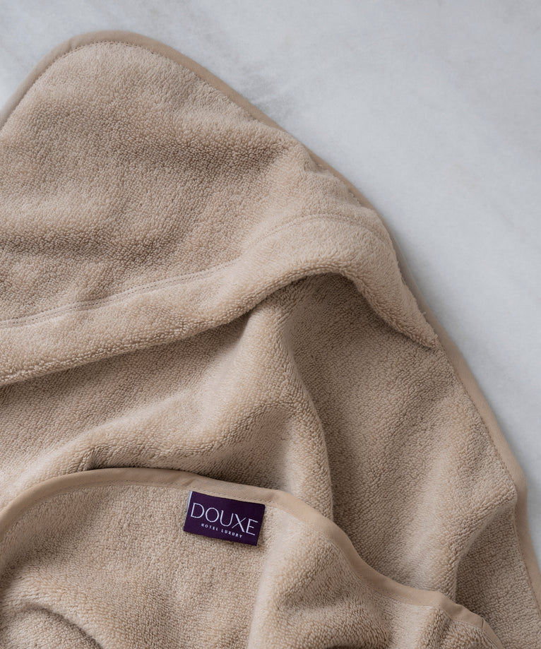 badcape baby in latte, detail shot van capuchon en DOUXE logo met marmeren achtergrond