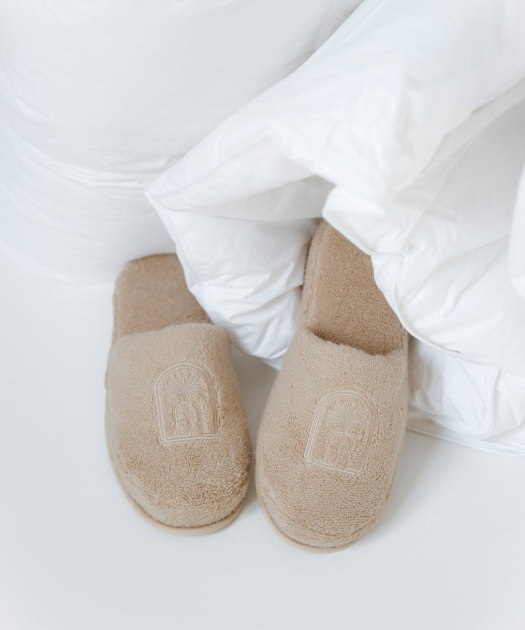 Badslippers in latte met DOUXE logo, liggend in een dekbed